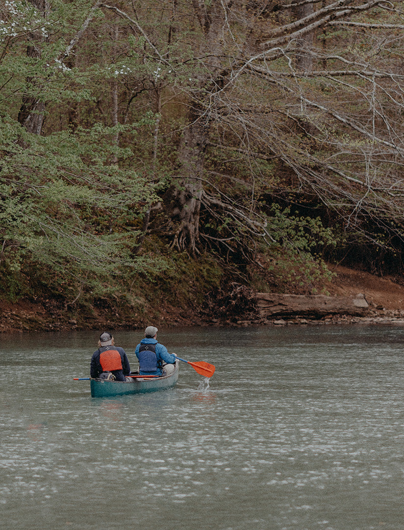 Two people wearing PFDs paddling a canoe down the Mulberry River.