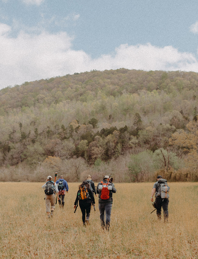 A Brewha Bushwhack competition team hikes across a field toward a forested hill.
