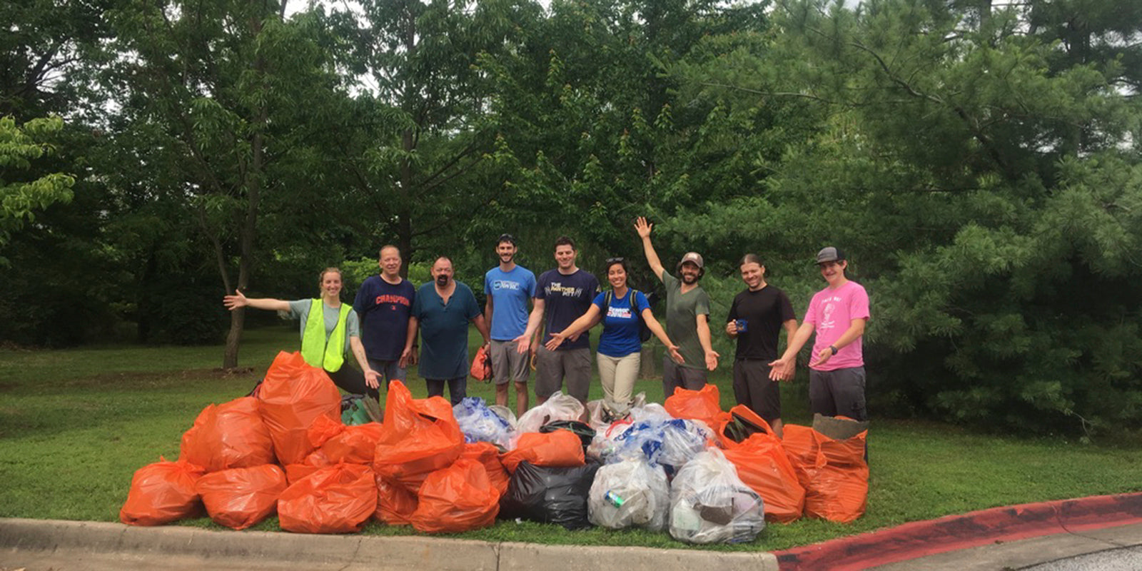 A group of people standing behind a collection of garbage and recycling bags.