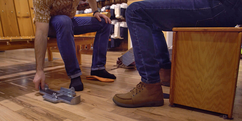 A sales clerk helps measure a customer's foot using a Brannock device.